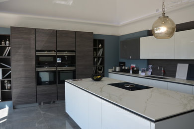 Photo of a large modern single-wall kitchen/diner in Essex with a submerged sink, ceramic flooring, an island, grey floors, flat-panel cabinets, white cabinets, brown splashback and black appliances.