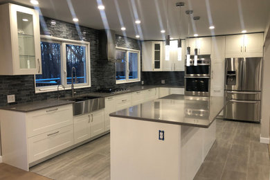 Eat-in kitchen - mid-sized modern l-shaped porcelain tile and gray floor eat-in kitchen idea in New York with a farmhouse sink, shaker cabinets, white cabinets, quartzite countertops, gray backsplash, glass tile backsplash, stainless steel appliances, an island and gray countertops