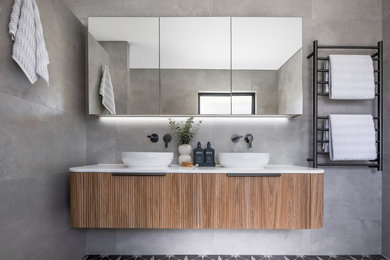 Inspiration for a large master bathroom in Perth with medium wood cabinets, a corner tub, an open shower, a one-piece toilet, gray tile, ceramic tile, grey walls, ceramic floors, grey floor, an open shower, white benchtops, a double vanity and a floating vanity.