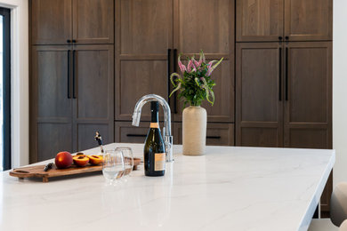 Example of a mid-sized transitional medium tone wood floor kitchen design in DC Metro with a single-bowl sink, flat-panel cabinets, quartz countertops, white backsplash, quartz backsplash, stainless steel appliances, an island and white countertops