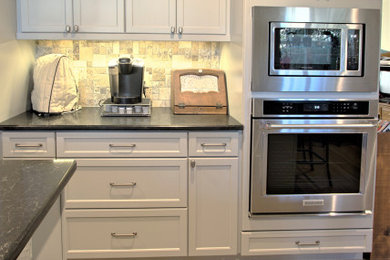 Inspiration for an eclectic eat-in kitchen in Dallas with white cabinets, multi-coloured splashback, limestone splashback, stainless steel appliances, with island, brown floor and black benchtop.