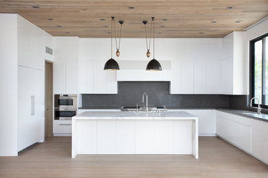 Inspiration for a large contemporary l-shaped light wood floor open concept kitchen remodel in Los Angeles with an undermount sink, flat-panel cabinets, white cabinets, limestone countertops, gray backsplash, stone slab backsplash, stainless steel appliances, an island and gray countertops