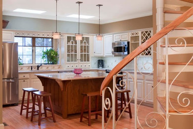 Inspiration for a mid-sized transitional l-shaped light wood floor open concept kitchen remodel in Philadelphia with an undermount sink, raised-panel cabinets, beige cabinets, granite countertops, white backsplash, ceramic backsplash, stainless steel appliances and an island