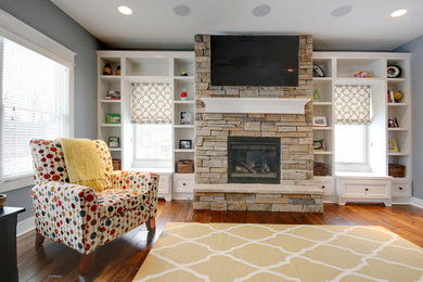 This is an example of a large arts and crafts open concept living room in Grand Rapids with grey walls, medium hardwood floors, a standard fireplace, a stone fireplace surround and a wall-mounted tv.