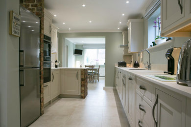Medium sized traditional kitchen/diner in Oxfordshire with an integrated sink, shaker cabinets, beige cabinets, black appliances, porcelain flooring, a breakfast bar and beige floors.