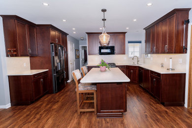 Example of a mid-sized classic u-shaped medium tone wood floor and brown floor eat-in kitchen design in Baltimore with an undermount sink, shaker cabinets, dark wood cabinets, quartz countertops, white backsplash, quartz backsplash, stainless steel appliances, an island and white countertops
