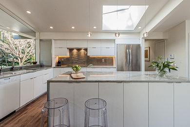 Large contemporary l-shaped eat-in kitchen in Seattle with an undermount sink, flat-panel cabinets, white cabinets, quartzite benchtops, grey splashback, glass tile splashback, white appliances, light hardwood floors, with island and brown floor.