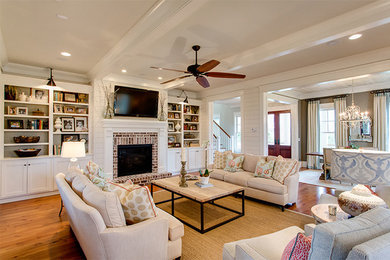 Large elegant open concept medium tone wood floor living room photo in Charleston with white walls, a standard fireplace, a brick fireplace and a wall-mounted tv