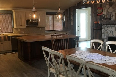 Inspiration for a large country l-shaped dark wood floor and gray floor open concept kitchen remodel in Las Vegas with a farmhouse sink, raised-panel cabinets, white cabinets, wood countertops, gray backsplash, subway tile backsplash, stainless steel appliances and an island