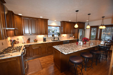 Inspiration for a large timeless u-shaped dark wood floor and brown floor eat-in kitchen remodel in Denver with an undermount sink, raised-panel cabinets, dark wood cabinets, granite countertops, beige backsplash, porcelain backsplash, stainless steel appliances and an island