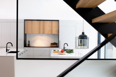 Example of a large trendy single-wall medium tone wood floor kitchen design in Montreal with an undermount sink, flat-panel cabinets, gray cabinets, quartz countertops, white backsplash, quartz backsplash, paneled appliances, two islands and white countertops