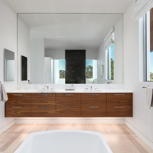 Freestanding bathtub - large modern master light wood floor and brown floor freestanding bathtub idea in Tampa with flat-panel cabinets, dark wood cabinets, white walls, a drop-in sink, marble countertops and white countertops