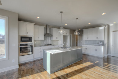 Example of a large transitional l-shaped medium tone wood floor and brown floor eat-in kitchen design in Kansas City with an undermount sink, shaker cabinets, white cabinets, granite countertops, gray backsplash, glass tile backsplash, stainless steel appliances, an island and white countertops