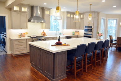 Photo of a large transitional l-shaped eat-in kitchen in Baltimore with a farmhouse sink, recessed-panel cabinets, grey cabinets, quartz benchtops, white splashback, stainless steel appliances, dark hardwood floors, with island, brown floor and white benchtop.