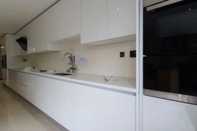 This is an example of a large modern grey and white single-wall open plan kitchen in West Midlands with a belfast sink, flat-panel cabinets, white cabinets, quartz worktops, beige splashback, integrated appliances, porcelain flooring, an island and white worktops.
