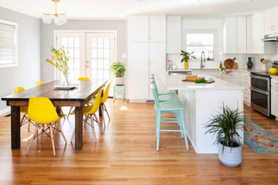 Photo of a small contemporary l-shaped kitchen/diner in Raleigh with a built-in sink, flat-panel cabinets, yellow cabinets, engineered stone countertops, white splashback, ceramic splashback, stainless steel appliances, medium hardwood flooring, an island, brown floors and white worktops.