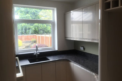 Photo of a small contemporary u-shaped enclosed kitchen in Other with a submerged sink, flat-panel cabinets, grey cabinets, quartz worktops, green splashback, glass sheet splashback, integrated appliances and laminate floors.