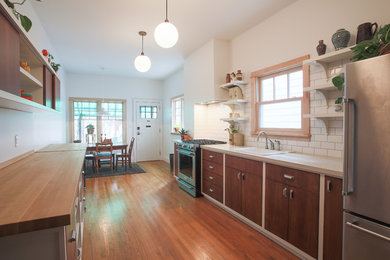 Inspiration for a transitional galley medium tone wood floor and brown floor eat-in kitchen remodel in Toronto with a drop-in sink, flat-panel cabinets, medium tone wood cabinets, white backsplash, subway tile backsplash, stainless steel appliances and no island