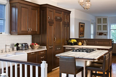 Mid-sized transitional l-shaped eat-in kitchen in Seattle with a farmhouse sink, recessed-panel cabinets, dark wood cabinets, marble benchtops, white splashback, stainless steel appliances, with island, subway tile splashback, medium hardwood floors and brown floor.