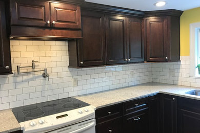 Example of a mid-sized classic u-shaped dark wood floor and brown floor enclosed kitchen design in New York with a double-bowl sink, raised-panel cabinets, dark wood cabinets, white backsplash, subway tile backsplash, stainless steel appliances, a peninsula, beige countertops and granite countertops