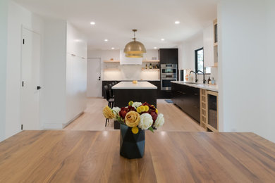 Photo of a large modern u-shaped kitchen in San Francisco with a submerged sink, flat-panel cabinets, black cabinets, engineered stone countertops, white splashback, engineered quartz splashback, integrated appliances, light hardwood flooring, an island and white worktops.