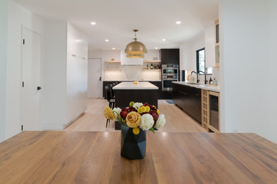 Example of a large minimalist u-shaped light wood floor kitchen design in San Francisco with an undermount sink, flat-panel cabinets, black cabinets, quartz countertops, white backsplash, quartz backsplash, paneled appliances, an island and white countertops