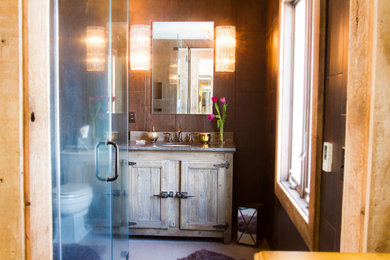 Mid-sized mountain style master brown tile and pebble tile porcelain tile corner shower photo in New York with an undermount sink, recessed-panel cabinets, distressed cabinets, soapstone countertops, a one-piece toilet and brown walls
