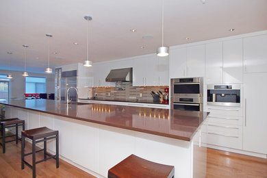 This is an example of a large contemporary galley eat-in kitchen in Calgary with an undermount sink, flat-panel cabinets, white cabinets, solid surface benchtops, multi-coloured splashback, glass tile splashback, stainless steel appliances, light hardwood floors and with island.