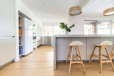 Design ideas for a mid-sized contemporary eat-in kitchen in Perth with flat-panel cabinets, white cabinets, concrete benchtops, stainless steel appliances, light hardwood floors, with island and white splashback.