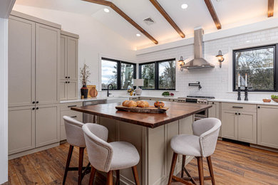 Inspiration for a mid-sized transitional u-shaped vinyl floor, brown floor and vaulted ceiling kitchen remodel in Other with a farmhouse sink, raised-panel cabinets, beige cabinets, quartz countertops, white backsplash, ceramic backsplash, stainless steel appliances, an island and white countertops