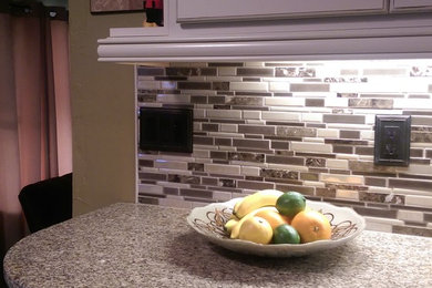 Eat-in kitchen - mid-sized transitional l-shaped laminate floor eat-in kitchen idea in Other with an undermount sink, raised-panel cabinets, white cabinets, granite countertops, multicolored backsplash, mosaic tile backsplash, white appliances and no island