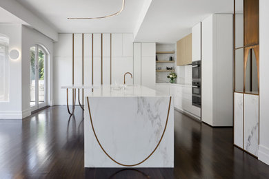Design ideas for a large contemporary l-shaped eat-in kitchen in Melbourne with an undermount sink, white cabinets, marble benchtops, white splashback, ceramic splashback, black appliances, medium hardwood floors, with island, brown floor and white benchtop.