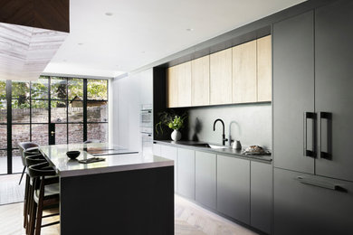 Medium sized contemporary galley kitchen/diner in London with an integrated sink, flat-panel cabinets, black cabinets, composite countertops, black splashback, engineered quartz splashback, black appliances, light hardwood flooring, an island, brown floors, black worktops, a drop ceiling and feature lighting.