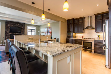 Open concept kitchen - large traditional l-shaped porcelain tile and beige floor open concept kitchen idea in Other with a double-bowl sink, recessed-panel cabinets, dark wood cabinets, granite countertops, beige backsplash, glass tile backsplash, stainless steel appliances and a peninsula