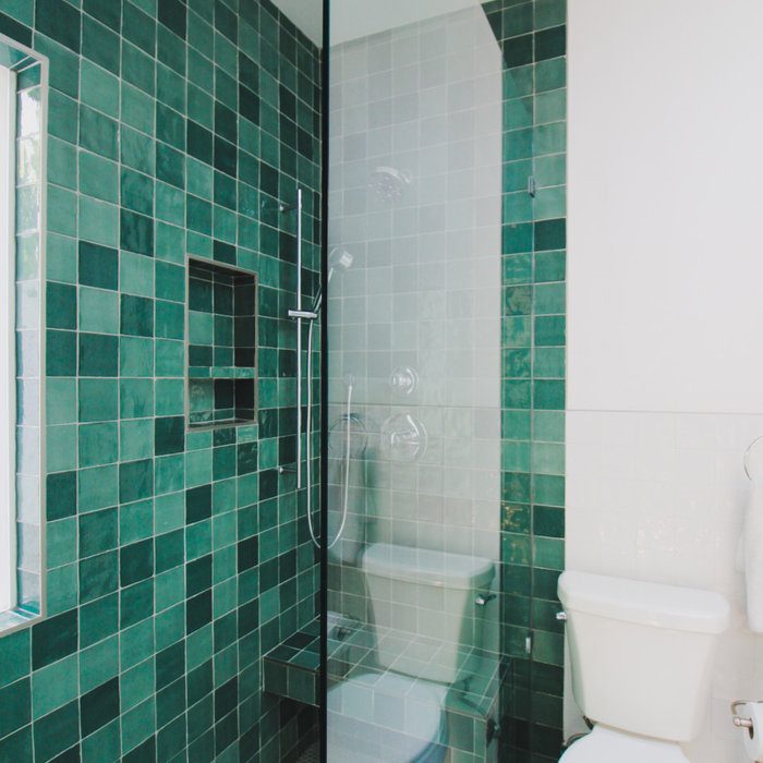 Bathroom in ADU located in in Eagle Rock, CA. Green shower wall tiles with gray mosaic styled shower floor tiles. The clear glass shower has a boarderless frame and is completed with a niche for all o