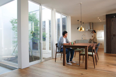 Modelo de comedor moderno abierto sin chimenea con paredes blancas, suelo de madera clara y suelo marrón