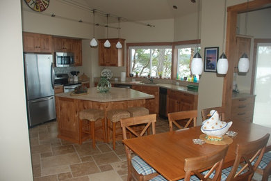 Eat-in kitchen - mid-sized coastal u-shaped travertine floor eat-in kitchen idea in Seattle with an undermount sink, raised-panel cabinets, medium tone wood cabinets, solid surface countertops, multicolored backsplash, stone tile backsplash, stainless steel appliances and an island