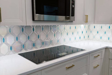 Example of a mid-sized transitional eat-in kitchen design in New York with shaker cabinets, white cabinets, quartzite countertops, white backsplash, glass tile backsplash, black appliances, an island and white countertops