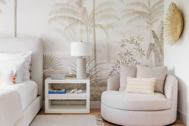 Imagen de dormitorio principal, blanco y beige y rosa costero de tamaño medio con paredes blancas, papel pintado, suelo de madera en tonos medios y suelo marrón