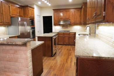 Eat-in kitchen - large traditional u-shaped medium tone wood floor eat-in kitchen idea in Dallas with an undermount sink, raised-panel cabinets, medium tone wood cabinets, granite countertops, beige backsplash, stone tile backsplash, stainless steel appliances and an island