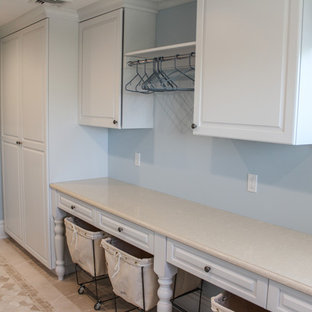 ニューヨークの大きいシャビーシック調のおしゃれな家事室 (ドロップインシンク、白いキャビネット、青い壁、セラミックタイルの床、左右配置の洗濯機・乾燥機、レイズドパネル扉のキャビネット) の写真