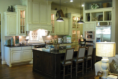Large elegant l-shaped medium tone wood floor open concept kitchen photo in Austin with an undermount sink, raised-panel cabinets, white cabinets, quartz countertops, beige backsplash, stone tile backsplash, stainless steel appliances and an island