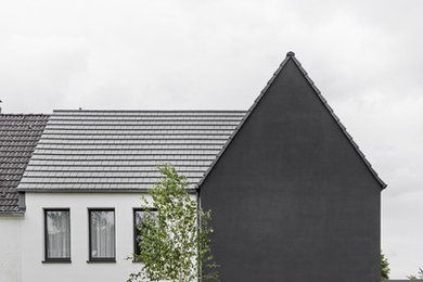 Design ideas for a modern stucco black house exterior in Essen with a gable roof and a tile roof.