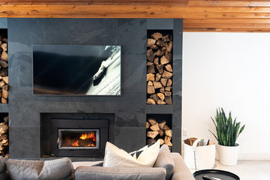 This is an example of a contemporary living room in Toronto with concrete floors, a wood stove, white walls, a tile fireplace surround, a wall-mounted tv and white floor.