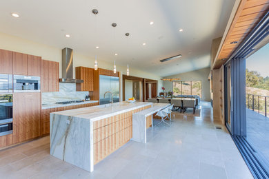 Large contemporary galley open plan kitchen in San Francisco with an undermount sink, flat-panel cabinets, medium wood cabinets, marble benchtops, white splashback, marble splashback, stainless steel appliances, porcelain floors, with island and beige floor.