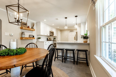 Example of a mid-sized cottage l-shaped ceramic tile and gray floor eat-in kitchen design in Philadelphia with quartzite countertops, white countertops, a farmhouse sink, shaker cabinets, white cabinets, glass tile backsplash and stainless steel appliances