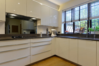 Mid-sized contemporary u-shaped eat-in kitchen in Other with a single-bowl sink, flat-panel cabinets, white cabinets, quartzite benchtops, white splashback, glass sheet splashback, panelled appliances, medium hardwood floors and no island.