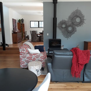 Diseño de sala de estar abierta, minimalista, grande, con paredes grises, suelo de madera en tonos medios, estufa de leña, televisor en una esquina y suelo marrón