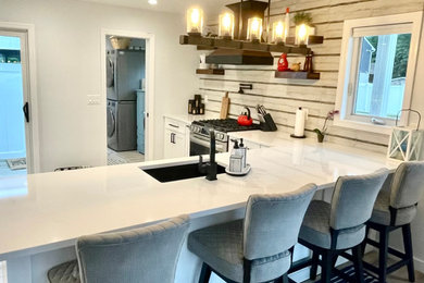 Example of a mid-sized transitional l-shaped laminate floor and beige floor open concept kitchen design in New York with an undermount sink, shaker cabinets, white cabinets, quartz countertops, multicolored backsplash, stainless steel appliances, a peninsula and white countertops