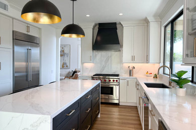 Large transitional u-shaped vinyl floor and brown floor kitchen photo in Orange County with an undermount sink, shaker cabinets, white cabinets, quartz countertops, white backsplash, quartz backsplash, stainless steel appliances, an island and white countertops